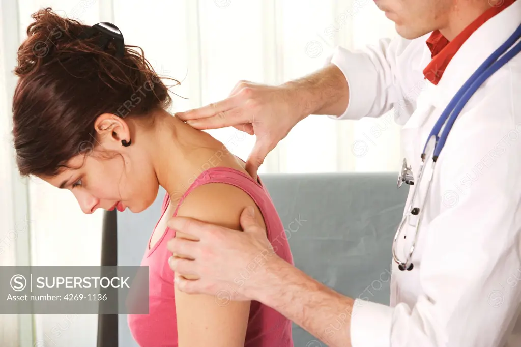 A doctor examines the backbone of a 20 years old patient palpating the cervical vertebras.