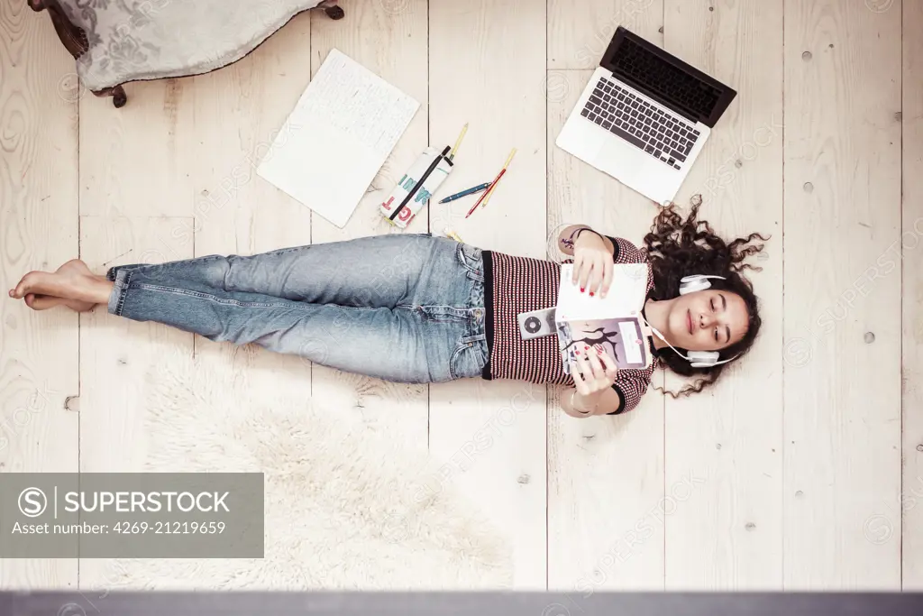 Teanage girl reading a book and listening to music.