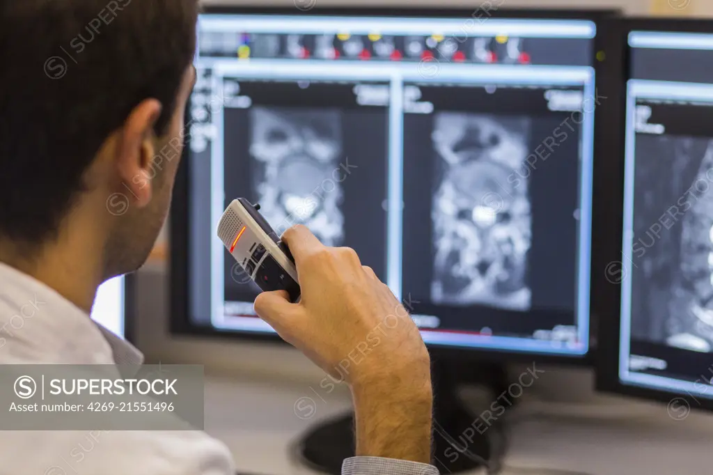 Doctor examines rachis MRI while recording notes on a dictaphone.