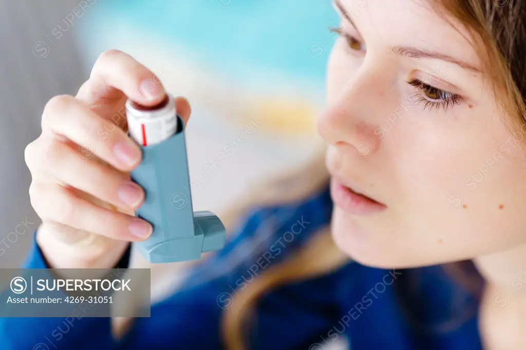 Asthma. Woman using an aerosol inhaler that contains bronchodilator for the treatment of asthma. The inhaler dilates lungs airways to improve breathing.