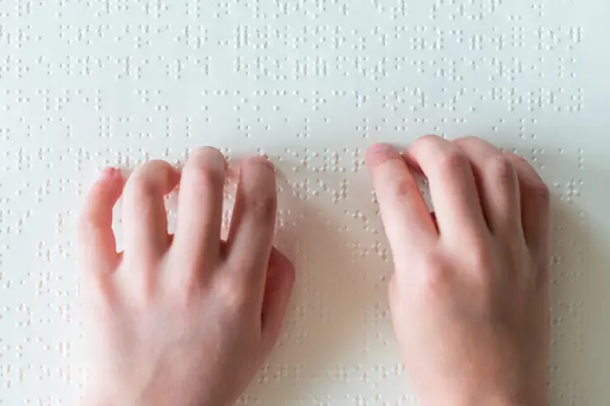 Hands of a blind child reading braille.