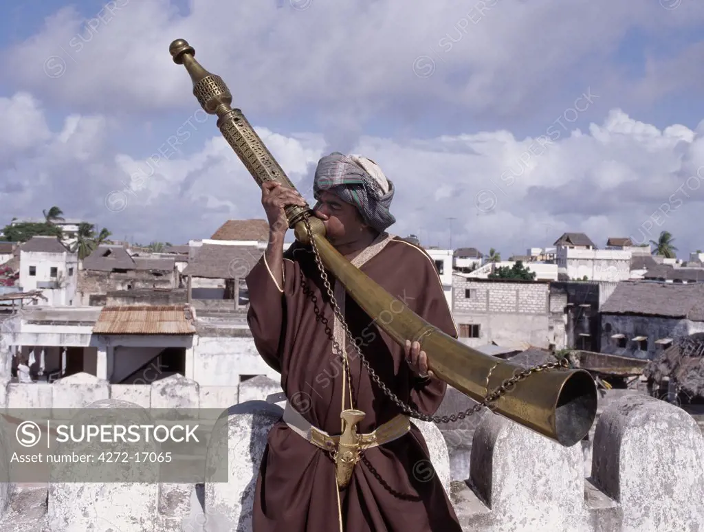 A Swahili man in traditional attire blows the Siwa on the