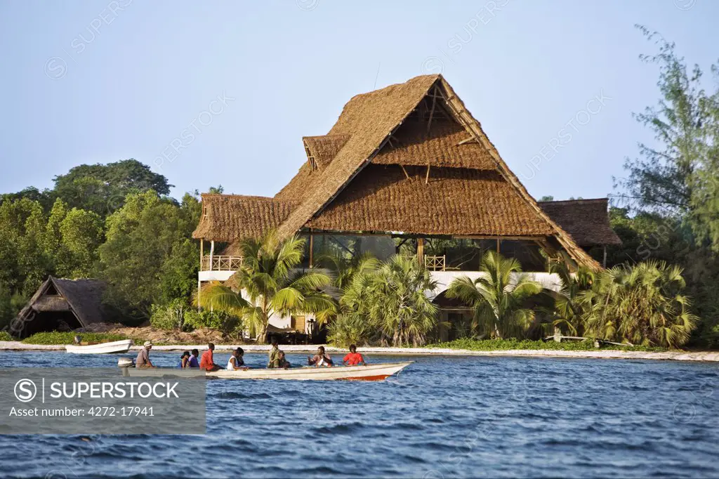 Kenya, Mombasa. Passengers being ferried to Funzi Island, off Kenyas south coast, pass an elegant house made of local material with coconut palm thatch roof.