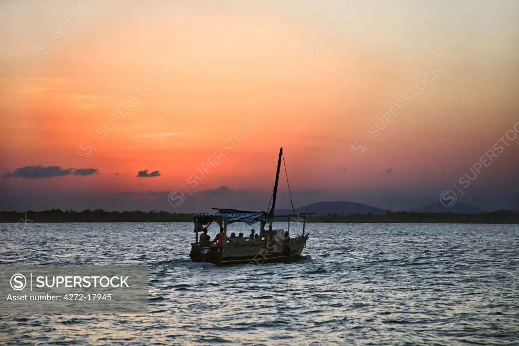 Kenya, Mombasa. As the last rays of the setting sun turn the sky a brilliant red, Residents of Funzi Island, off Kenyas south coast, take the ferry back to the mainland.