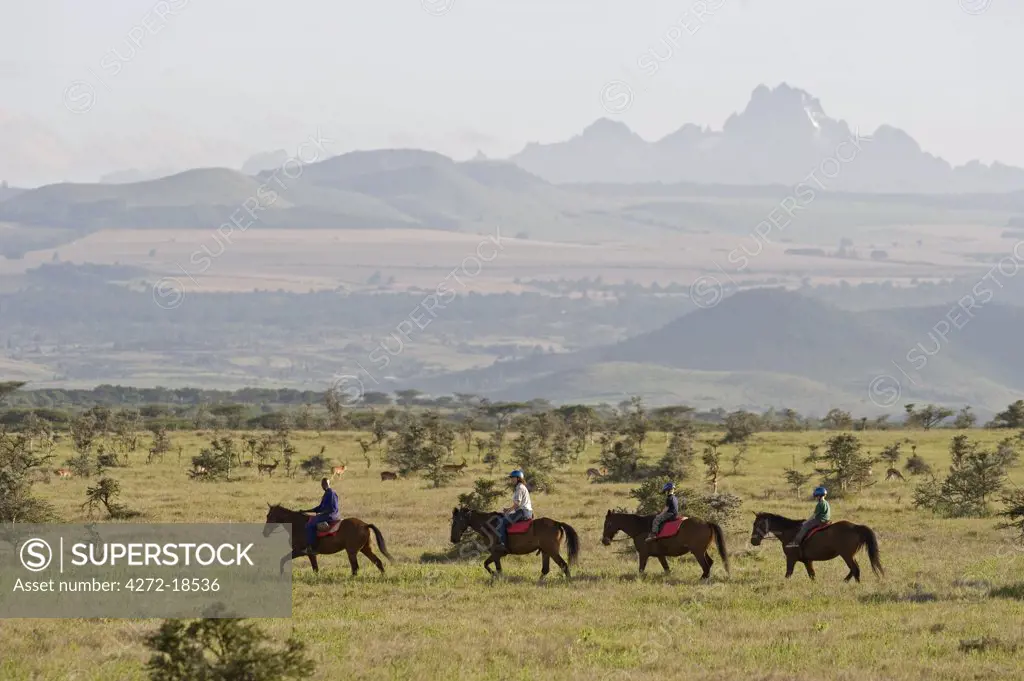 Kenya, Laikipia, Lewa Downs.  A family on a horse riding safari with Mount Kenya in the background.