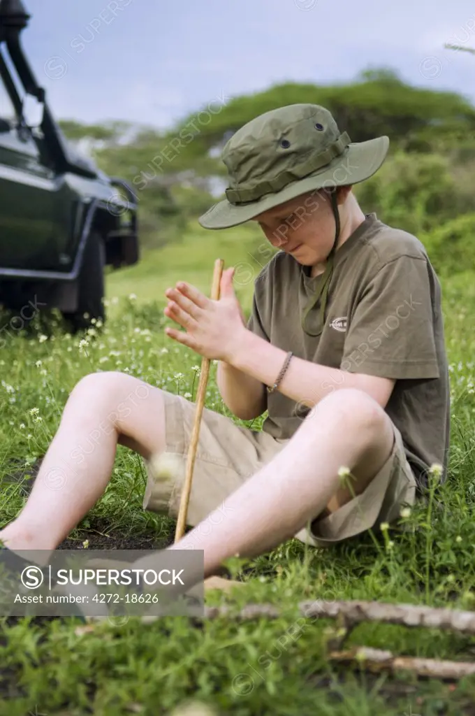 Kenya, Chyulu Hills, Ol Donyo Wuas.  A boy on safari practises lighting a fire the traditional way.  (MR)