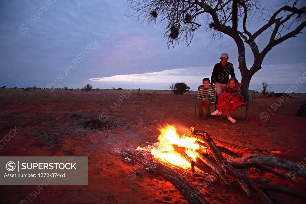 Family gathered around campfire in Tsavo East National Park, Kenya.