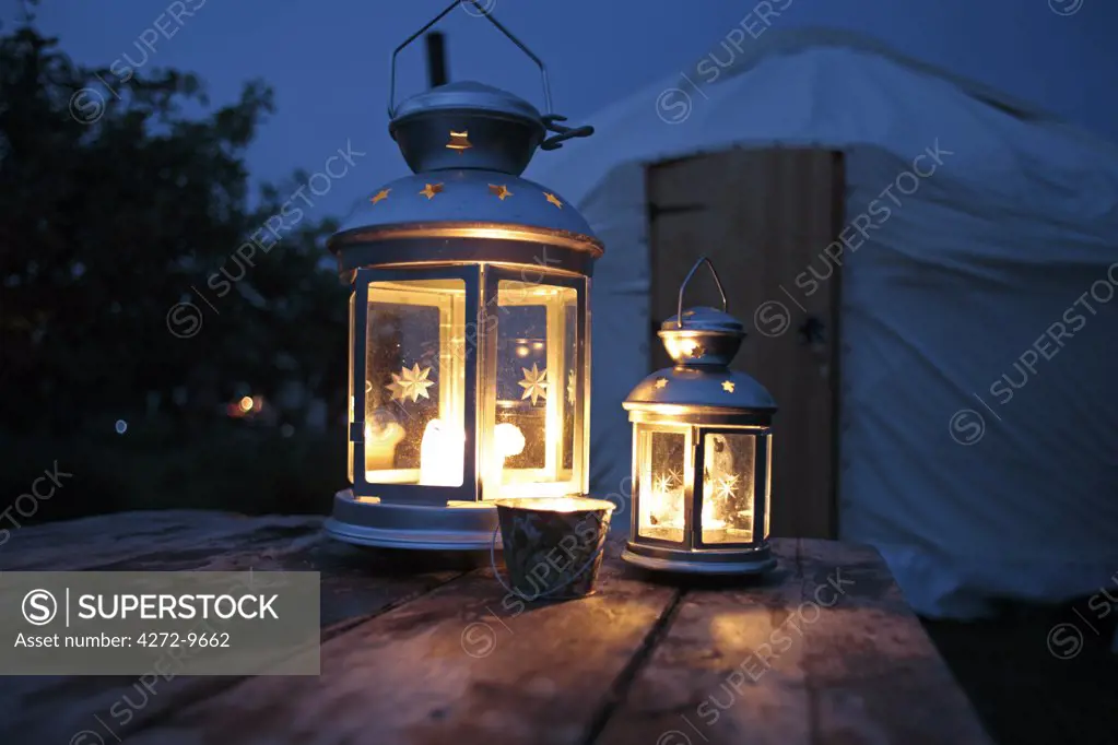 England, Isle of Wight. Candle lanterns on a table with a yurt in the background; Island Yurts near Freshwater Bay.