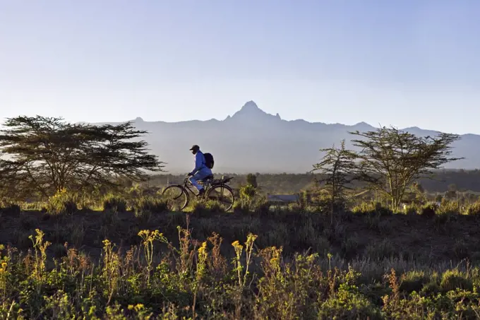 Kenya,Timau. In the early morning, a man cycles to work with Mount Kenya towering in the background.