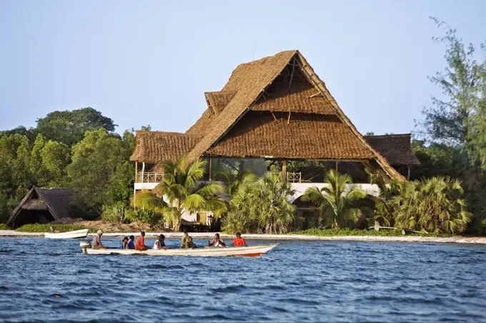 Kenya, Mombasa. Passengers being ferried to Funzi Island, off Kenyas south coast, pass an elegant house made of local material with coconut palm thatch roof.