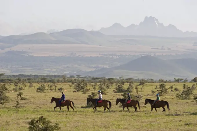 Kenya, Laikipia, Lewa Downs.  A family on a horse riding safari with Mount Kenya in the background.