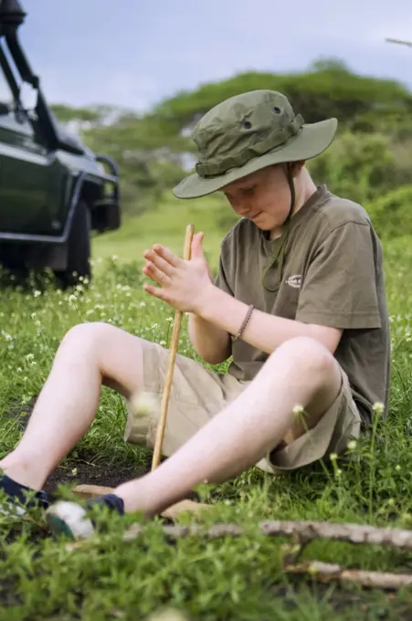 Kenya, Chyulu Hills, Ol Donyo Wuas.  A boy on safari practises lighting a fire the traditional way.  (MR)