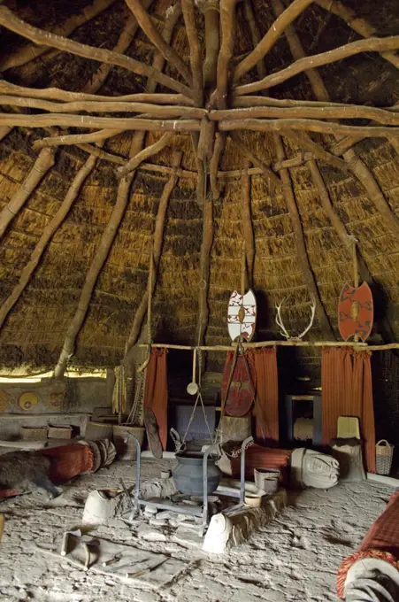 UK, Wales, Pembrokeshire. Interior of the re-created Chieftain's Hut, an Iron Age Celtic Roundhouse built on the original foundations , showing the fireplace, benches, sleeping area, thatched roof and wattle & daub walls at Castell Henlly, an Iron Age Fort near Newport.