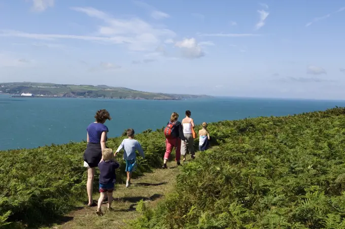 UK, Wales, Pembrokeshire. A family walks along the Pembrokeshire Coastal Path around Dinas Head with views of Fishguard Bay and Crincoed Point in the distance.