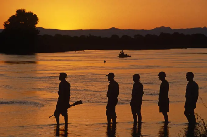 Walking safari from Bilimungwe Bushcamp cross the Kapamba River at sunset , Zambia