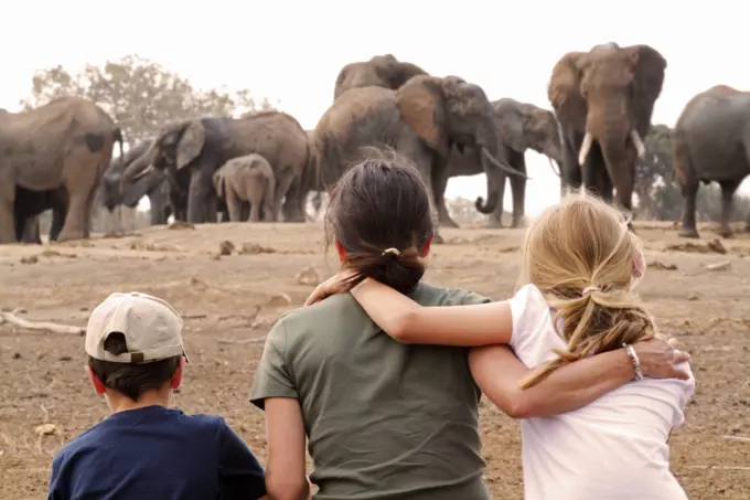 Family watching elephants at waterhole from Satao Camp in Tsavo East National Park, Kenya.