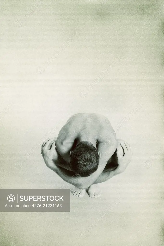 Nude man crouching with head down, hands on knees