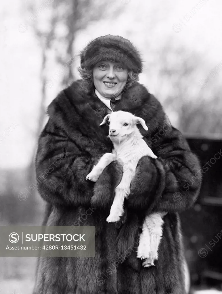 Woman in a fur coat and hat holding a small baby lamb in her arms All persons depicted are not longer living and no estate exists Supplier warranties ...