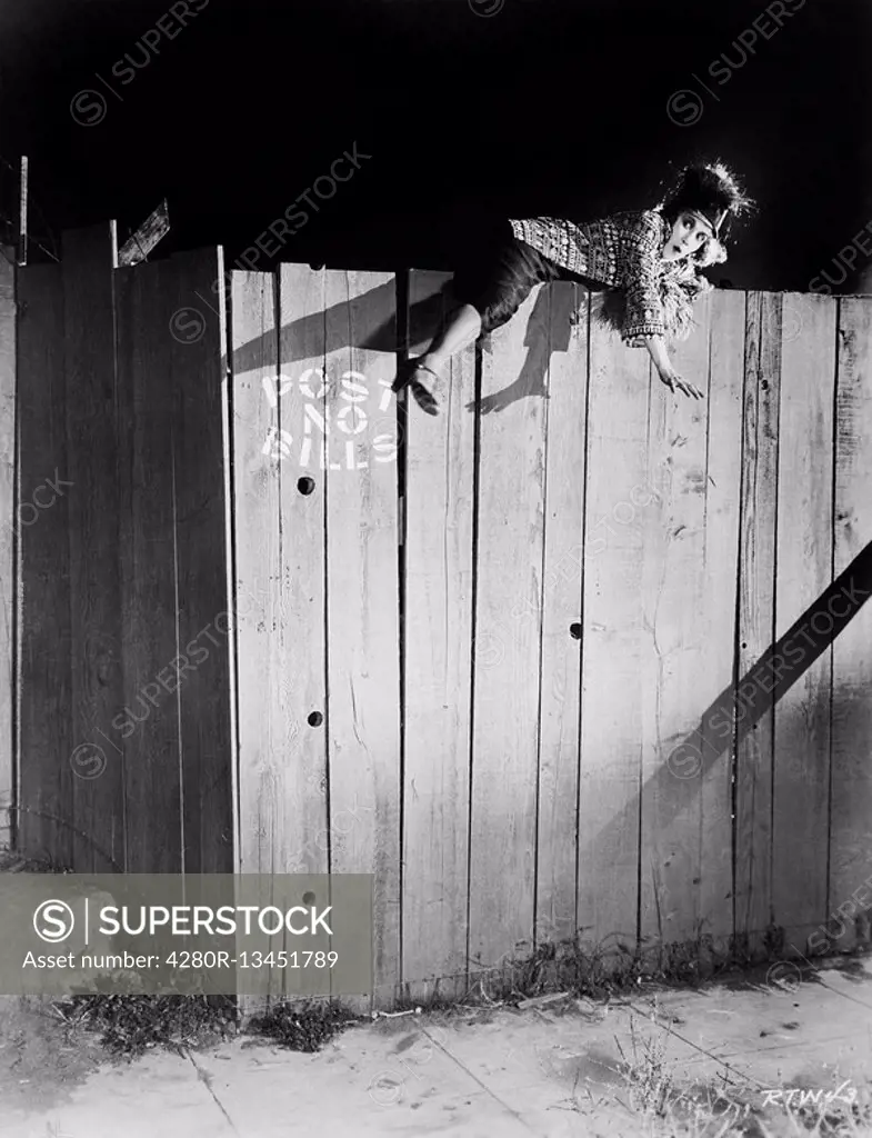 Young woman trying to climb over a wooden fence All persons depicted are not longer living and no estate exists Supplier warranties that there will be...