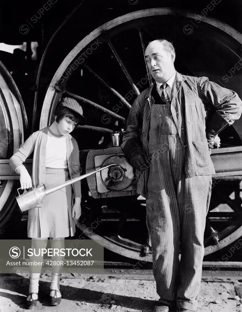 Little girl with an oil can standing next to a locomotive and the engine driver All persons depicted are not longer living and no estate exists Suppli...