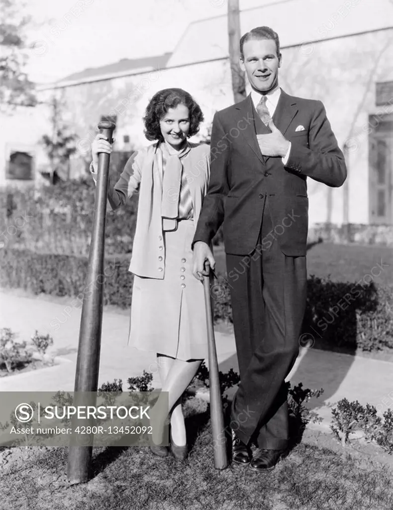 Couple standing together with one oversized baseball bat All persons depicted are not longer living and no estate exists Supplier warranties that ther...