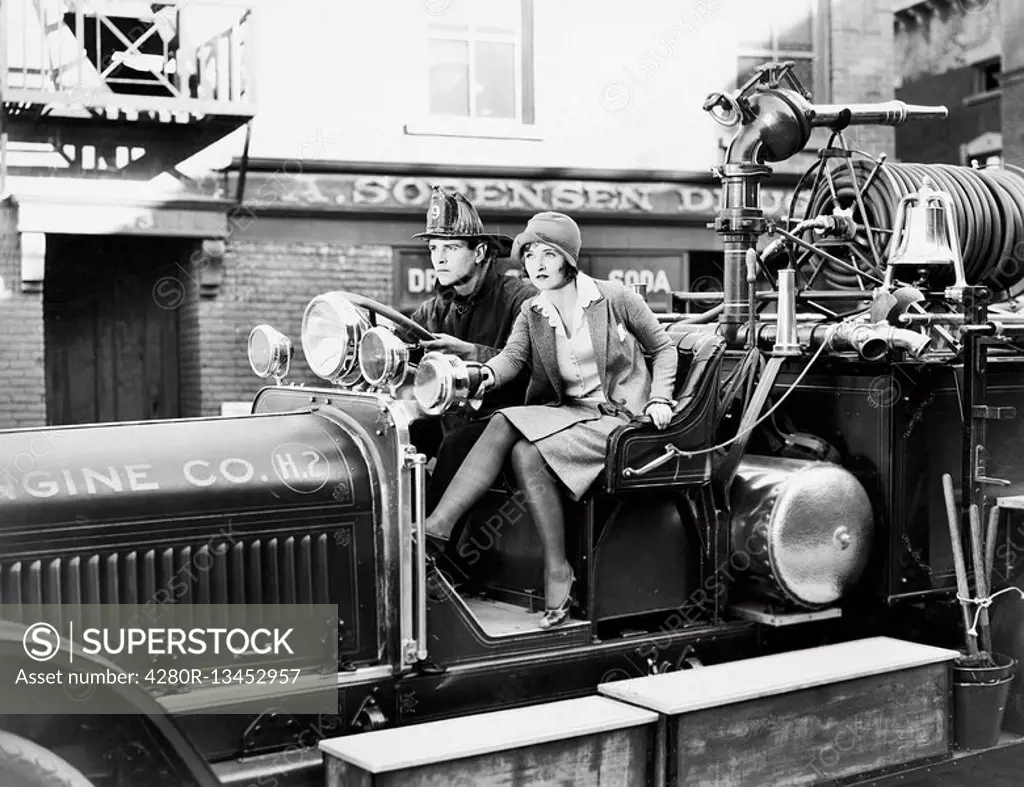 Firefighter driving a fire engine and a young woman sitting beside him All persons depicted are not longer living and no estate exists Supplier warran...