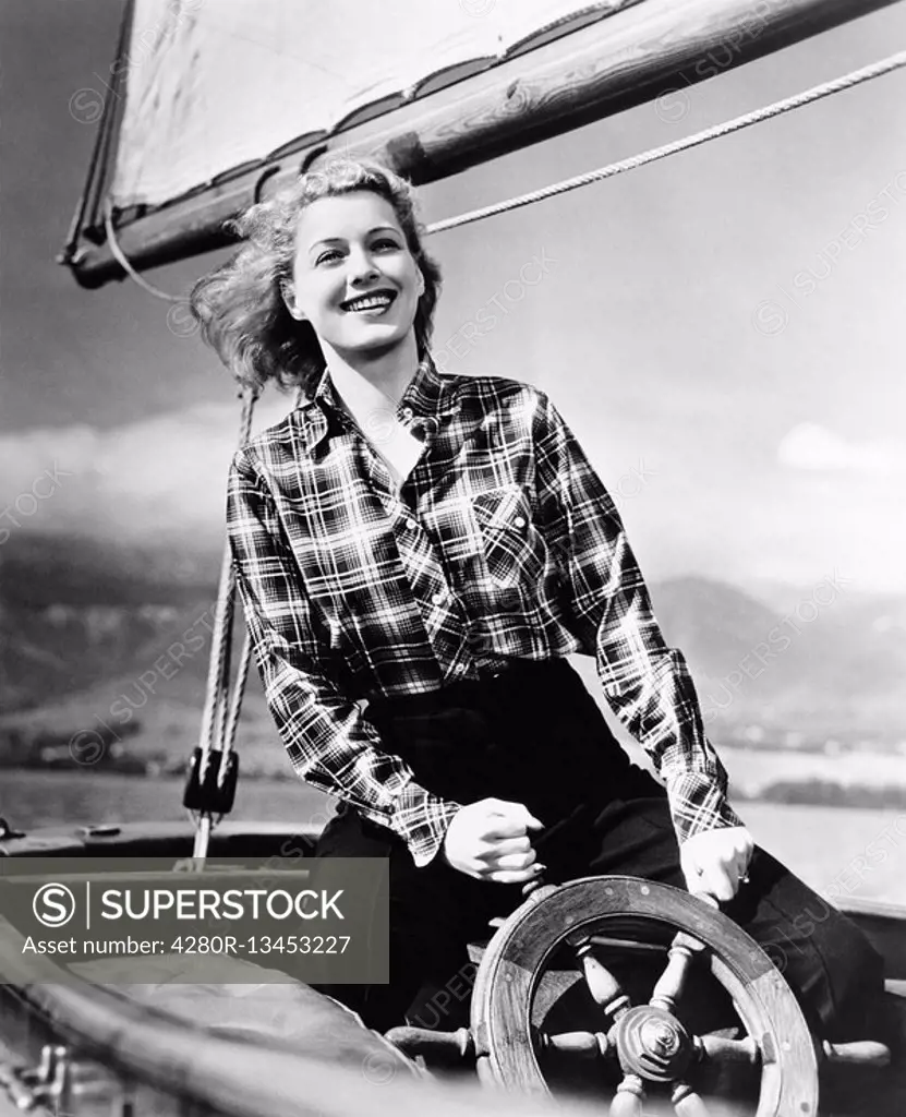 Young woman standing at the helm of a sailboat and holding the wheel All persons depicted are not longer living and no estate exists Supplier warranti...