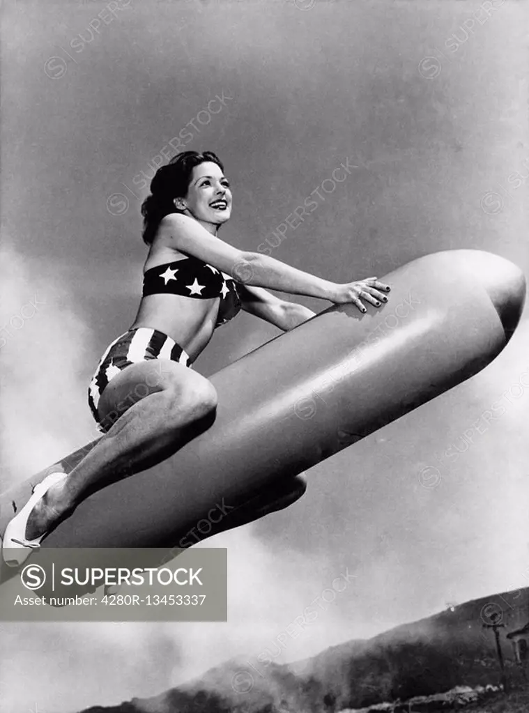 Low angle view of a young woman sitting on a rocket and smiling All persons depicted are not longer living and no estate exists Supplier warranties th...