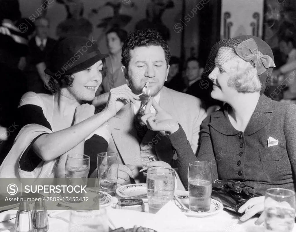 Two women lighting a cigarette for a man All persons depicted are not longer living and no estate exists Supplier warranties that there will be no mod...