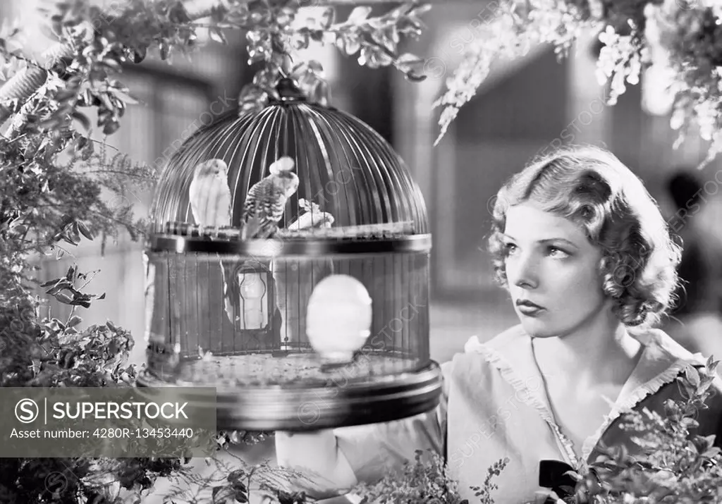 Woman looking into a bird cage with birds All persons depicted are not longer living and no estate exists Supplier warranties that there will be no mo...