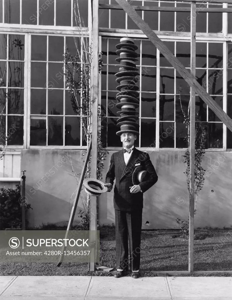 Man standing with stack of hats on head