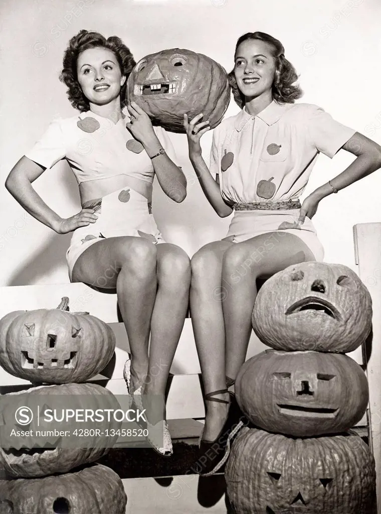 Two women sitting on fence with carved pumpkins