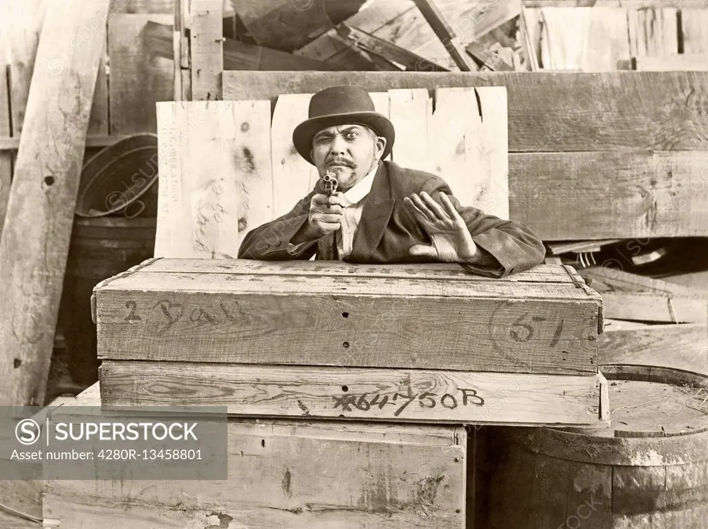 Cornered man behind wooden crates pointing gun