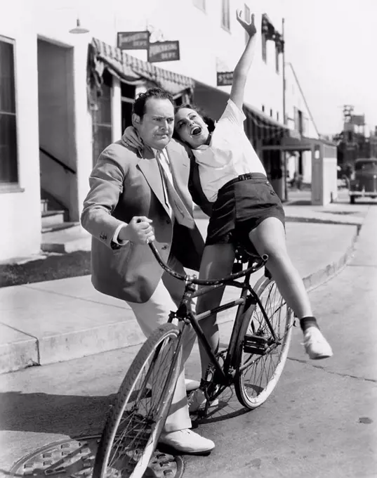 Man trying to balance an exuberant woman on a bicycle All persons depicted are not longer living and no estate exists Supplier warranties that there w...