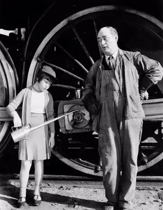 Little girl with an oil can standing next to a locomotive and the engine driver All persons depicted are not longer living and no estate exists Suppli...