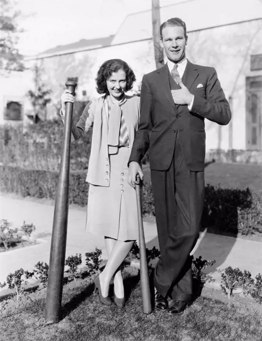 Couple standing together with one oversized baseball bat All persons depicted are not longer living and no estate exists Supplier warranties that ther...