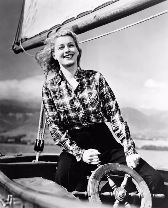 Young woman standing at the helm of a sailboat and holding the wheel All persons depicted are not longer living and no estate exists Supplier warranti...