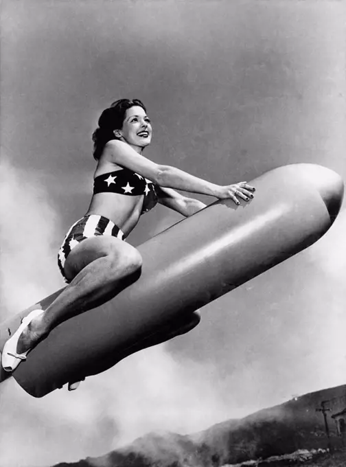 Low angle view of a young woman sitting on a rocket and smiling All persons depicted are not longer living and no estate exists Supplier warranties th...