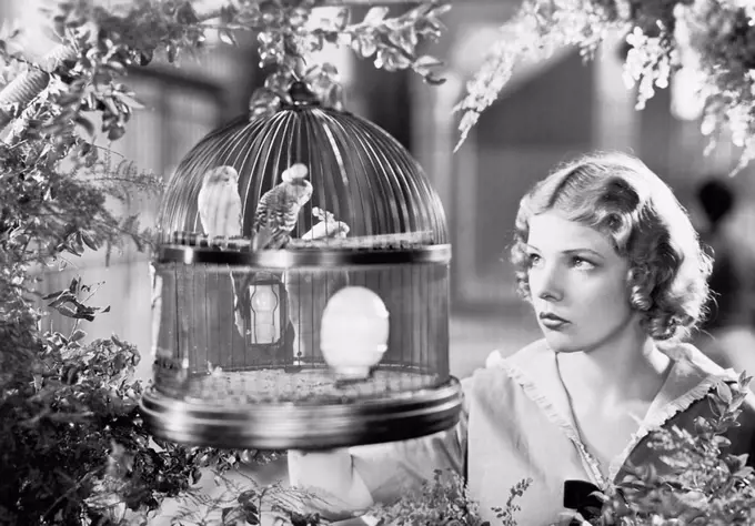 Woman looking into a bird cage with birds All persons depicted are not longer living and no estate exists Supplier warranties that there will be no mo...