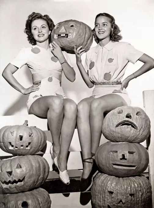 Two women sitting on fence with carved pumpkins