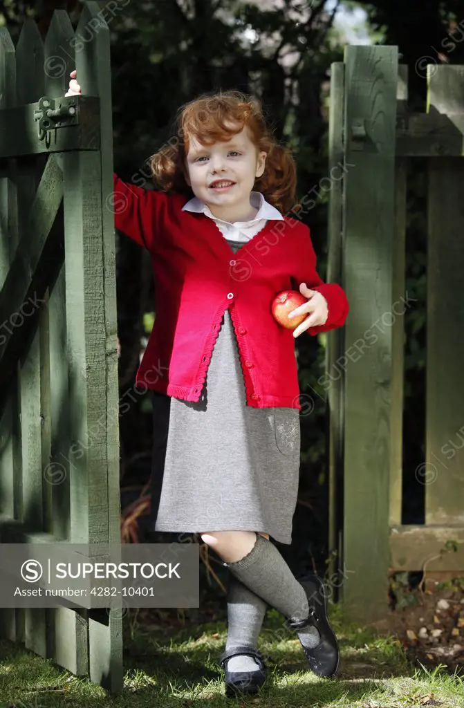 England. A young girl wearing school uniform holding an apple.