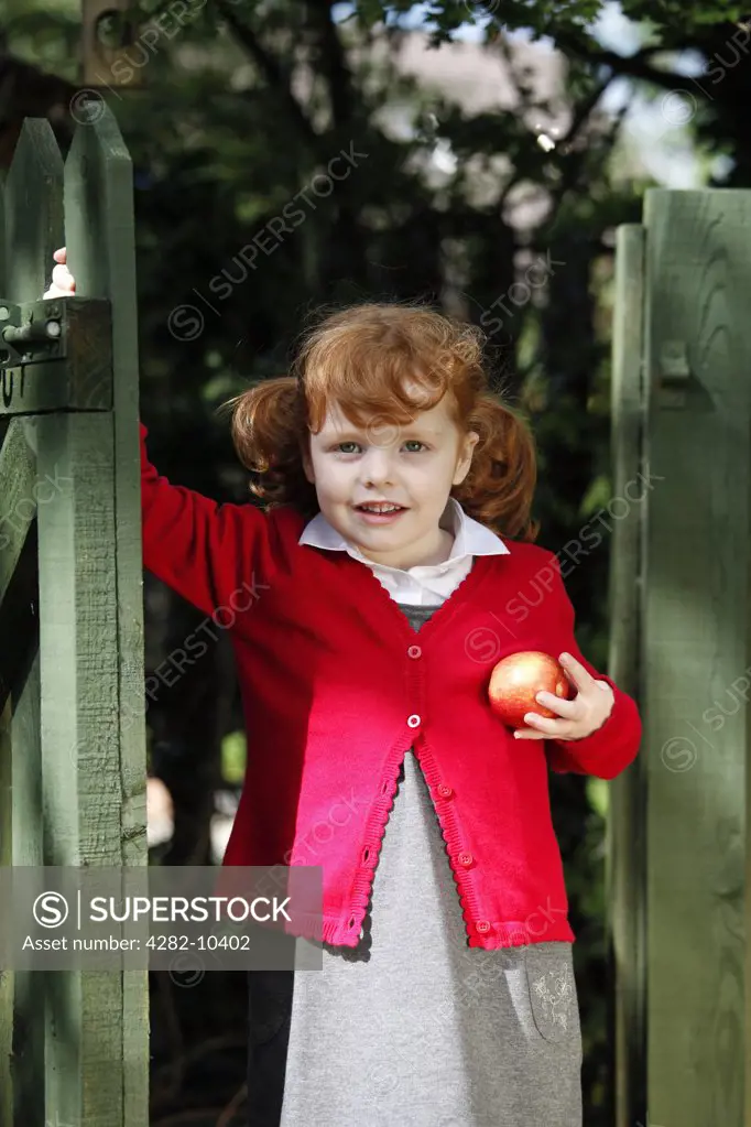 England. A young girl wearing school uniform holding an apple.