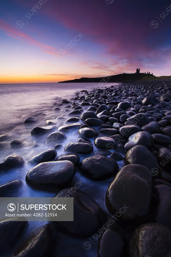 England, Northumberland, Embleton Bay. Waves crash againt the sea sculptured rocks dominating the coastline of Embleton Bay, overlooked by the dramatic ruins of Dunstanburgh Castle.