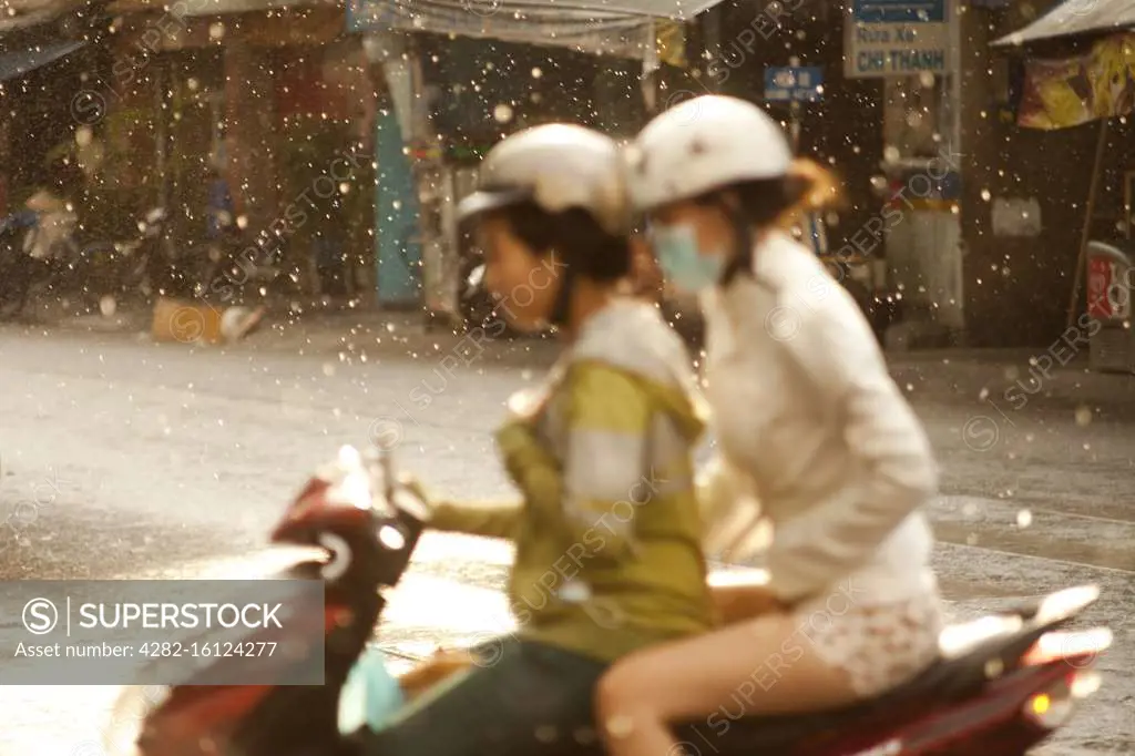 Two women share a moped during a rainstorm on the streets of Ho Chi Minh City in Vietnam.