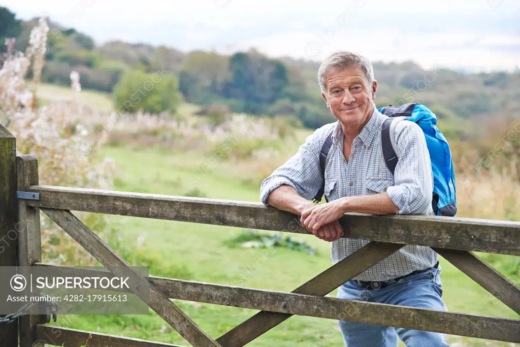 Portrait Of Senior Man On Hike In Countryside Resting By Gate