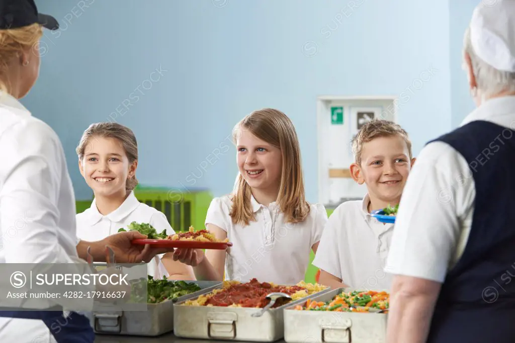 Pupils In School Cafeteria Being Served Lunch By Dinner Ladies