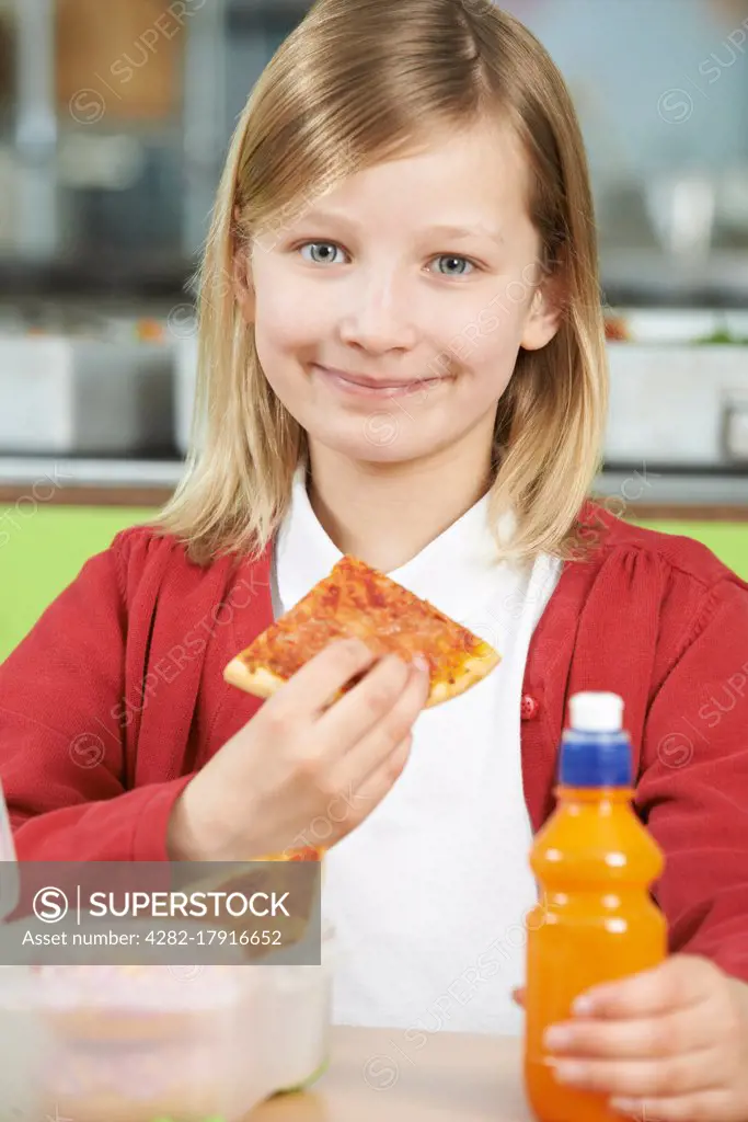 Girl Sitting At Table In School Cafeteria Eating Unhealthy Packed Lunch