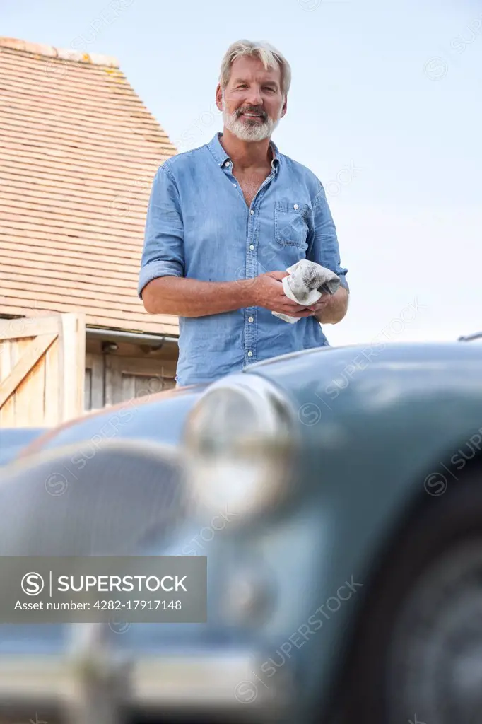 Portrait Of Mature Man Restoring Classic Sports Car Outdoors At Home