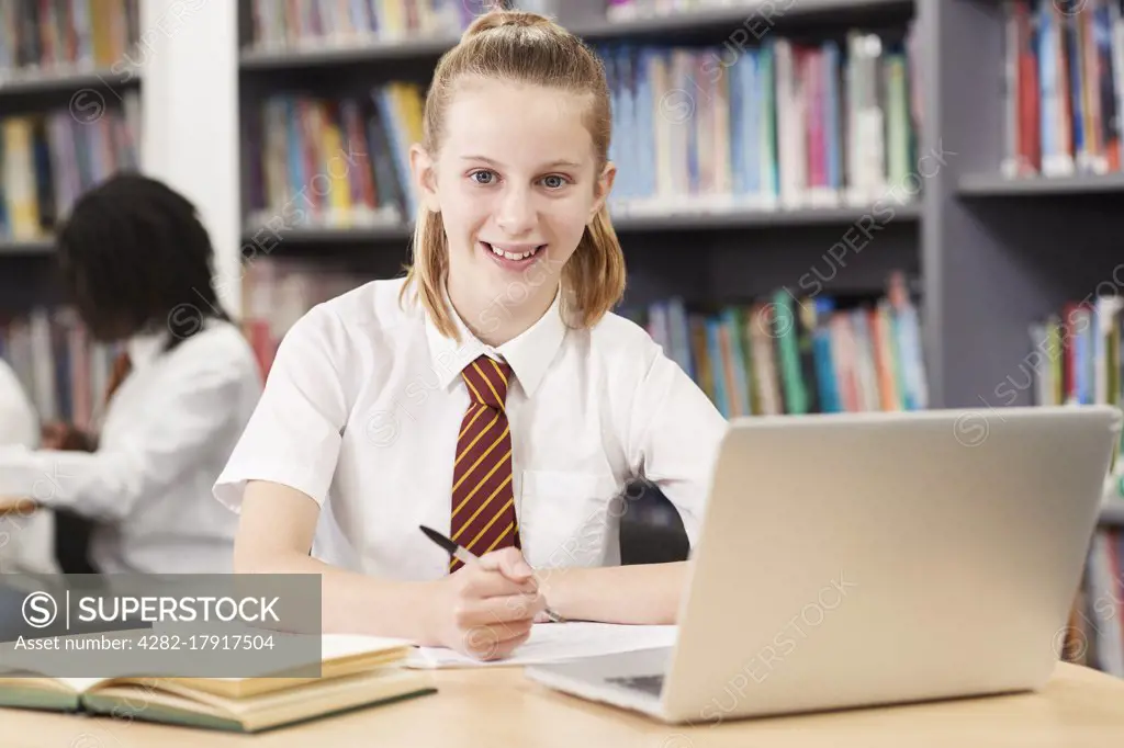 Portrait Of Female High School Student Wearing Uniform Working At Laptop In Library