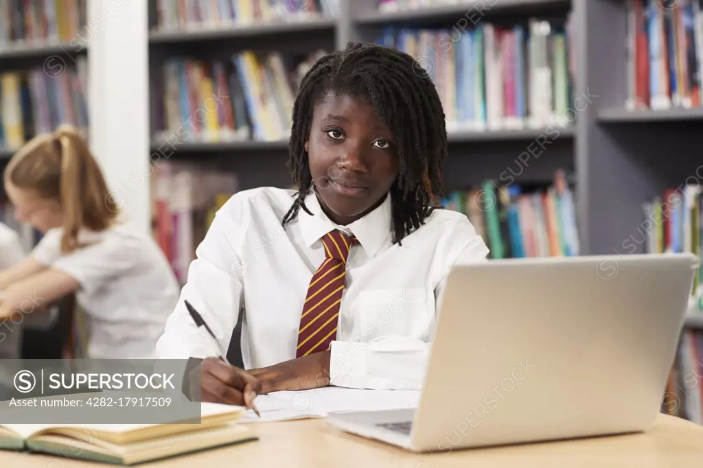 Portrait Of Female High School Student Wearing Uniform Working At Laptop In Library